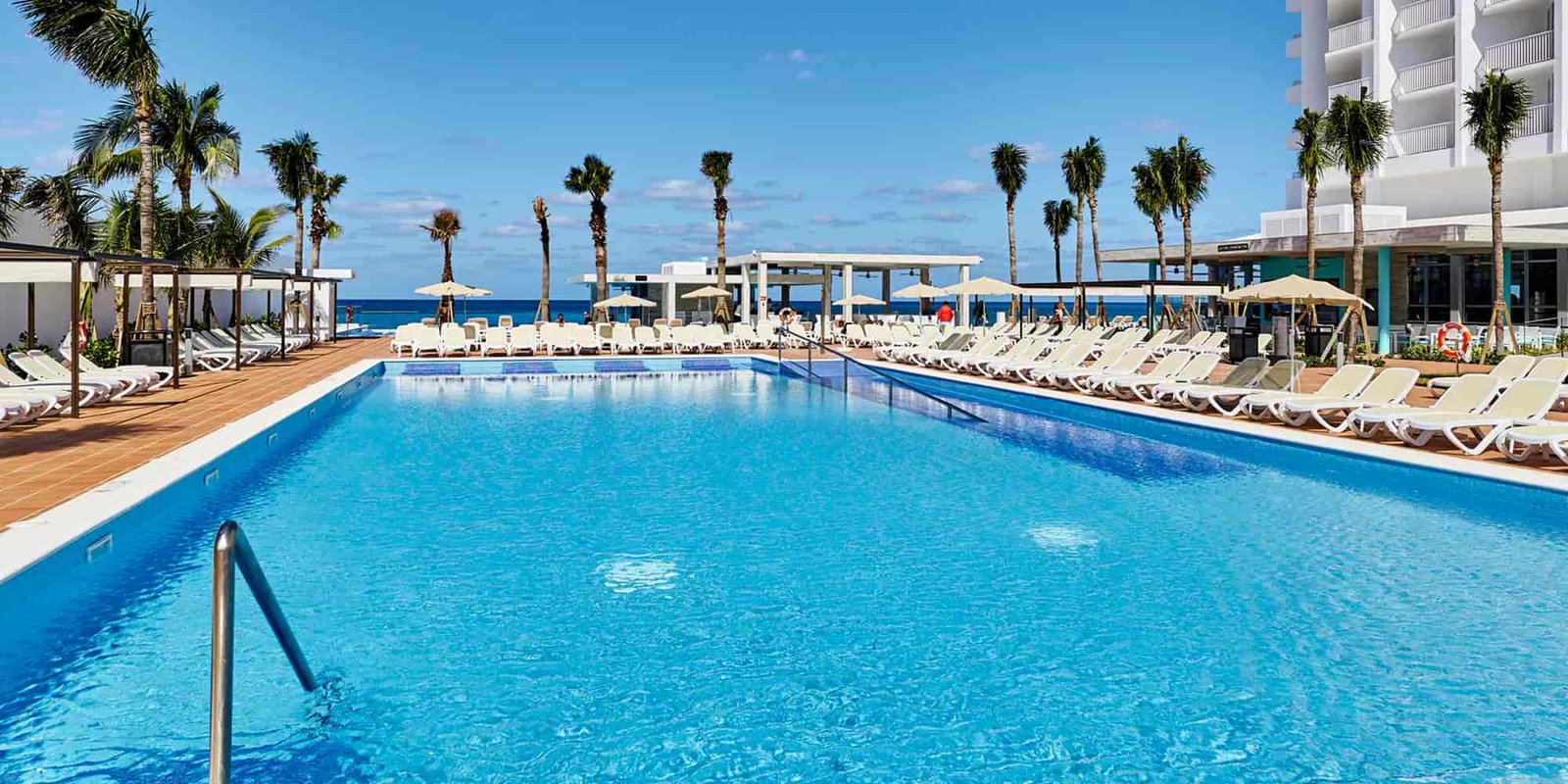 Sparkling blue pool lined with palms and sun loungers at Riu Palace Paradise Island